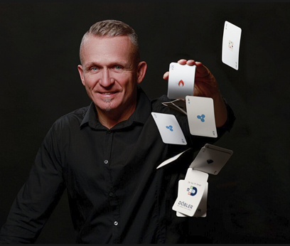 Ein Mann in einem schwarzen Hemd lächelt, während er vor einem dunklen Hintergrund gekonnt Spielkarten in die Luft wirft. Ein Mann in einem schwarzen Hemd lächelt, während er vor einem dunklen Hintergrund gekonnt Spielkarten in die Luft wirft.